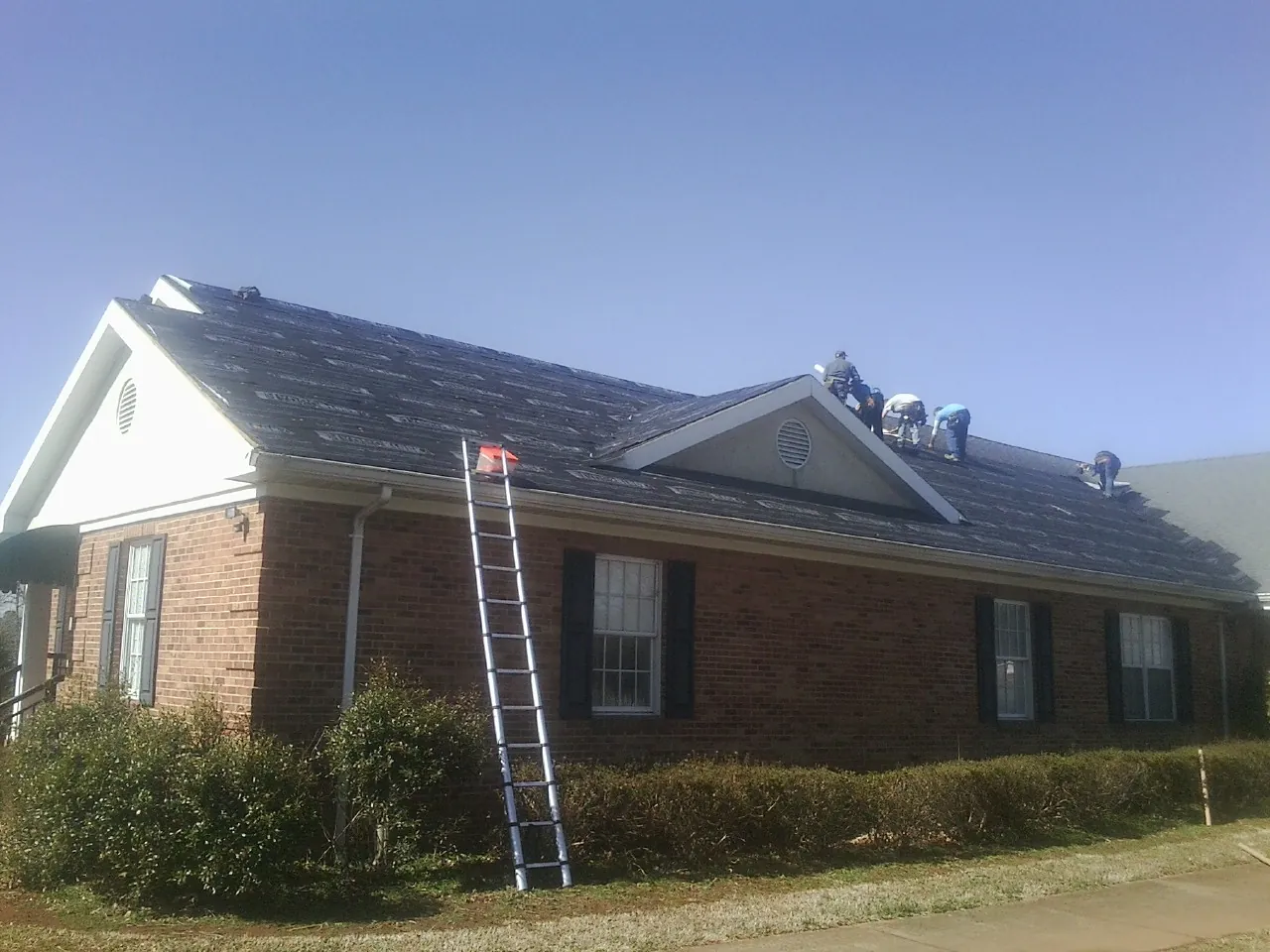 Crew tearing shingles off a brick ranch roof with a ladder set — Metal Roof Repair work by our crew in Modoc