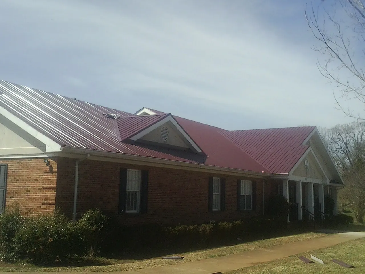 Red metal roof with gabled entries on a long brick building, from a Hail Damage Roof Repair job in Modoc