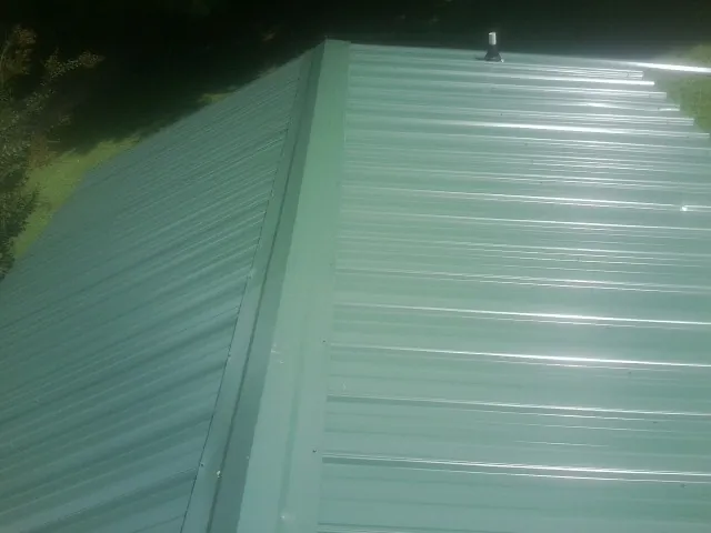 New green metal panels meeting at the ridge of a roof — Flat Roof Repair work by our crew in Modoc